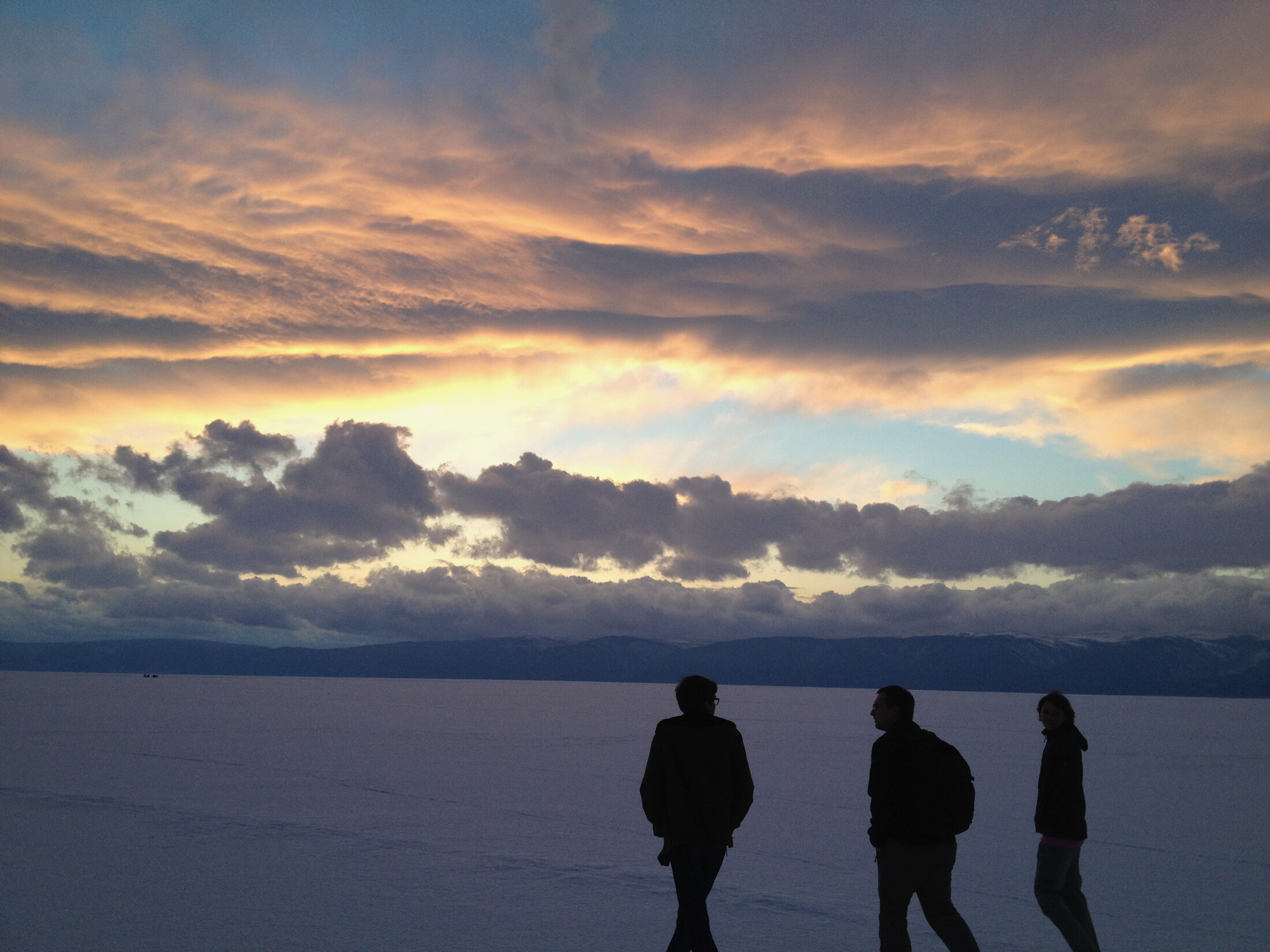 Three people walking into the sunset of lake Baikal